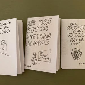 Op de afbeelding: Drie kleine, handgetekende zines met zwarte inkt op wit papier. De titels zijn: "Snowman Waits for the Elevator", "My Hat Keeps Getting Bigger" en "The Curse of the Wolf Man (1954)". Elk zine bevat eenvoudige illustraties en tekst.