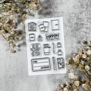 May include: Clear stamp set featuring various stationery-themed designs, including notebooks, stamps, and the text "Support My Local Stationery Store." The set also includes the text "I love paper and pens and inks and notebooks and journals and clips and pouches and stickers and stamps."