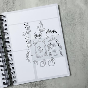 May include: A spiral-bound notebook with a white interior featuring black line art. The illustrations include a skull, candle, crystals, a window, and the word "Magic". The notebook is open, revealing the detailed drawings.