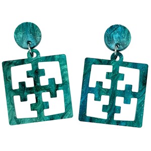 Puede incluir: Un par de pendientes de color azul turquesa con un diseño geométrico. Los pendientes están hechos de resina y tienen un efecto marmoleado.