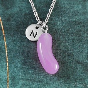 May include: A silver necklace with a purple jelly bean charm and a silver charm with the letter "N" on it.