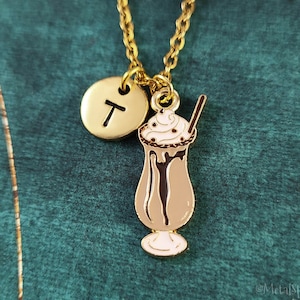 Puede incluir: Collar de oro con un dije de un batido de chocolate con crema batida y una pajita. El collar también tiene un pequeño dije redondo con la letra "T" en él.