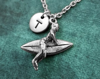 May include: Silver necklace with a surfer charm and a personalized initial disc. The initial disc is engraved with the letter "T".