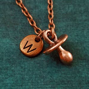 May include: A copper necklace with a small pacifier charm and a round charm with the letter "W" engraved on it.