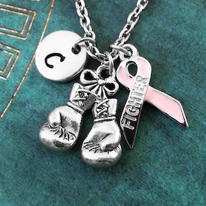 May include: Silver necklace with a pink ribbon charm, two boxing glove charms, and a letter 'C' charm. The ribbon charm has the word 'Fighter' on it.