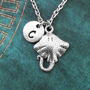 May include: Silver necklace with a charm of a stingray and a silver disc with the letter C.
