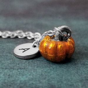 May include: A silver necklace with a small, orange pumpkin charm and a silver initial charm with the letter 'A'.