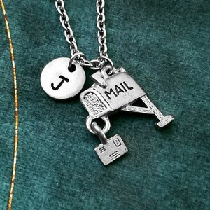 May include: A silver necklace with a silver mailbox charm, a letter charm, and a silver initial charm with the letter "J". The mailbox charm has the word "MAIL" on it.