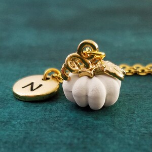 May include: A gold chain necklace with a white pumpkin charm and a gold initial charm with the letter "N".