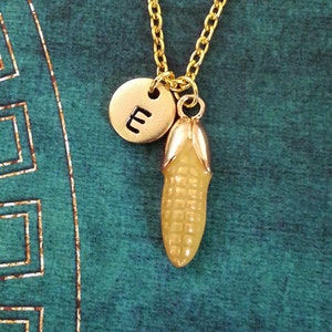 May include: Gold chain necklace with a small gold charm of an ear of corn and a gold disc charm with the letter "E" on it.