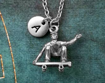 May include: Silver necklace with a charm of a person skateboarding and a silver disc charm with the letter A.