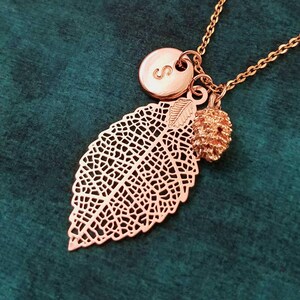 May include: Rose gold necklace featuring a delicate leaf charm, a small acorn charm, and a personalised initial charm with the letter "S".