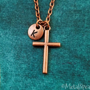 May include: A copper necklace with a small cross pendant and a round charm with the letter "K" engraved on it.