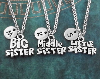 May include: Three silver necklaces with charms that say "Big Sister", "Middle Sister", and "Little Sister". Each necklace has a small silver disc with a letter on it: M, K, and S.