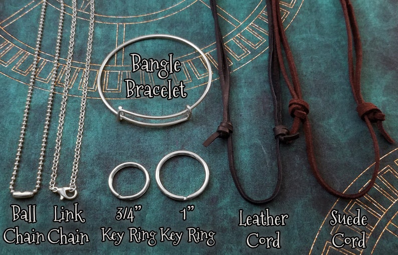 May include: A close-up of different types of jewellery chains and cords. The chains include a ball chain, a link chain, and a bangle bracelet. The cords include a leather cord and a suede cord. The chains and cords are labelled with their names and sizes. Bangle Bracelet, Ball Chain, Link Chain, 3/4" Key Ring, 1" Key Ring, Leather Cord, Suede Cord.