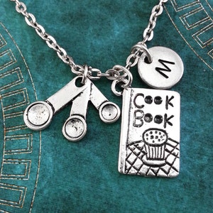 May include: Silver necklace with three measuring spoons, a cookbook charm, and a charm with the letter "M".