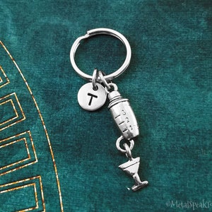 May include: Silver keyring with a letter T charm, a cocktail shaker charm, and a martini glass charm.