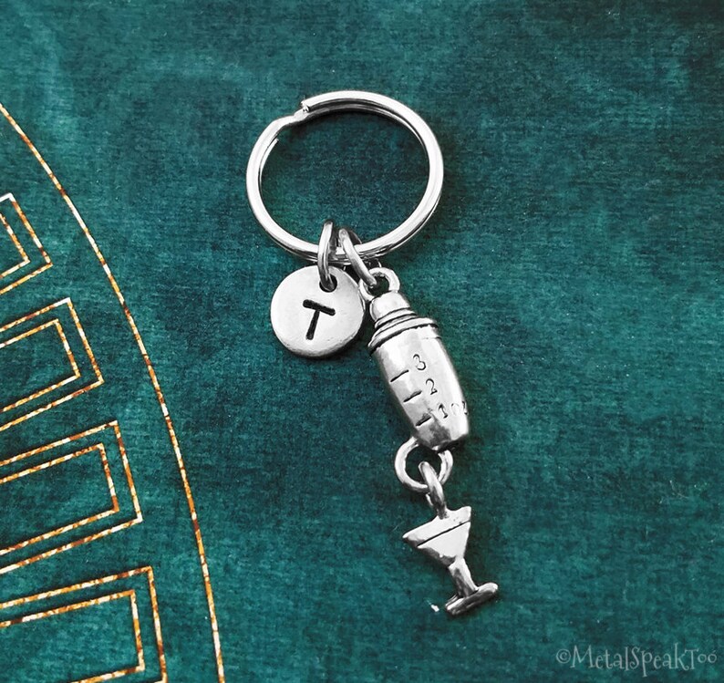May include: Silver keyring with a letter T charm, a cocktail shaker charm, and a martini glass charm.