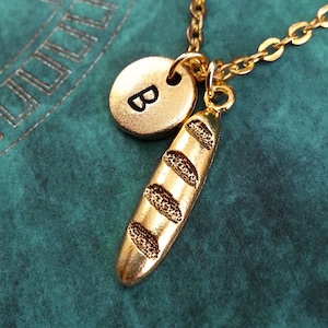 Könnte beinhalten: Goldkette mit einem Baguette-Anhänger und einem runden Anhänger mit dem Buchstaben "B" darauf.