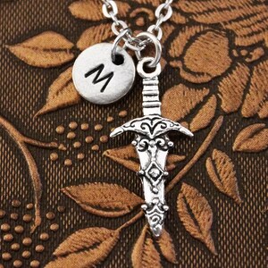 May include: Silver necklace with a sword charm and a silver initial charm with the letter "M".