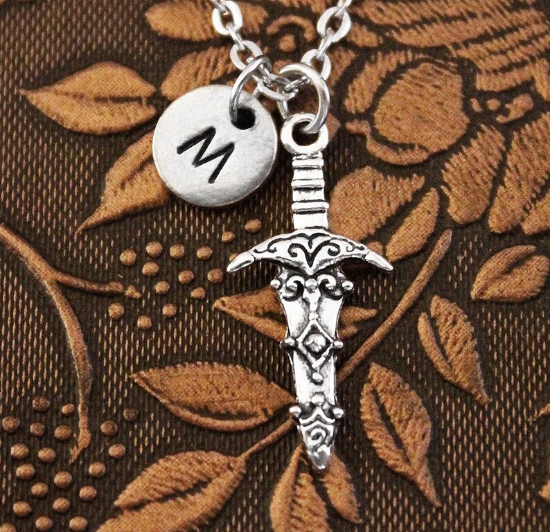 May include: Silver necklace with a sword charm and a silver initial charm with the letter "M".