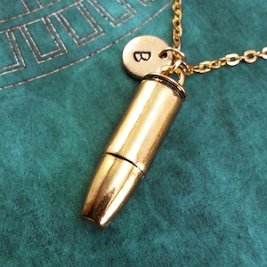 May include: Gold bullet casing necklace with a gold initial charm. The initial charm is a letter "B".
