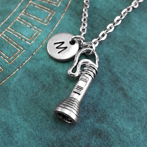 May include: A silver necklace with a flashlight charm and a silver charm with the letter 'M' on it.
