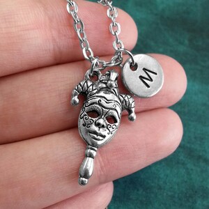 May include: Silver necklace with a jester mask charm and a silver charm with the letter 'M' on it.