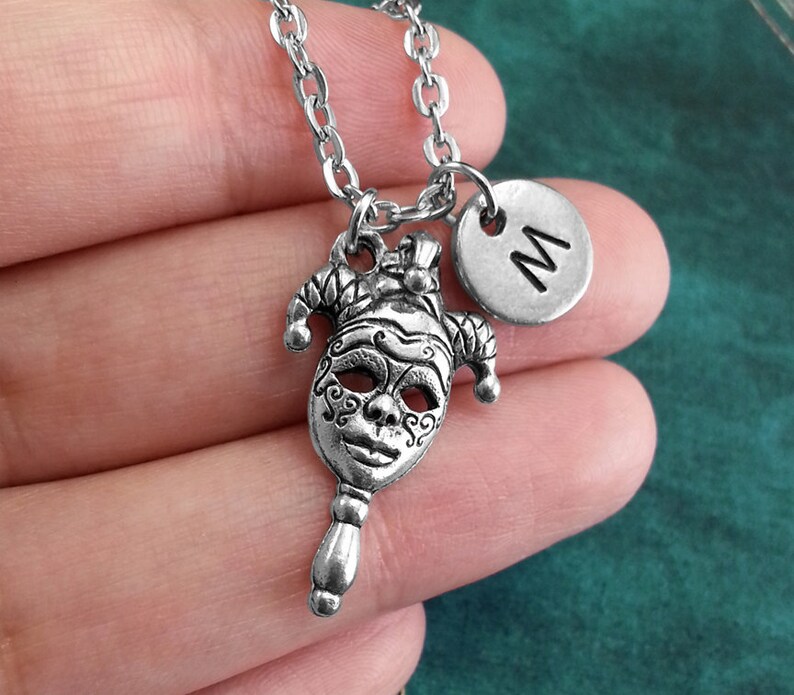 May include: Silver necklace with a jester mask charm and a silver charm with the letter 'M' on it.