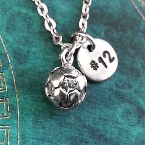 May include: Silver necklace with a soccer ball charm and a round charm with the number 12 on it.