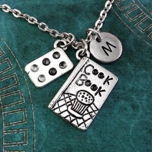 May include: Silver necklace with a cookbook charm, a charm with six dots, and a charm with the letter M.