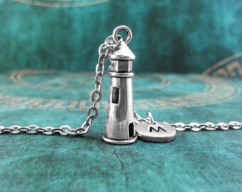May include: A silver necklace featuring a lighthouse charm and a silver charm with the letter "M" on it. The necklace is displayed against a teal backdrop.