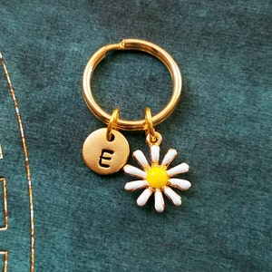 Pu&ograve; includere: Portachiavi dorato con un ciondolo a forma di margherita bianca e un ciondolo a disco dorato con la lettera "E" incisa.
