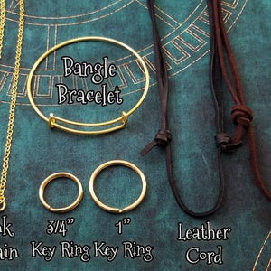 May include: A flat lay image showing different types of jewellery chains and cords. The chains include a ball chain, a link chain, a 3/4 inch key ring, and a 1 inch key ring. The cords include a black leather cord and a brown suede cord. The text "Bangle Bracelet" is written in the center of the image.