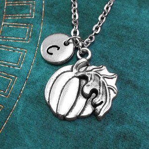 May include: A silver necklace with a pumpkin charm and a silver initial charm with the letter "C".