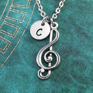 May include: Silver necklace featuring a treble clef charm and a small round charm with the letter C.