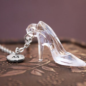 May include: A clear glass slipper charm with a silver chain and a silver charm with the letter "M" on it.
