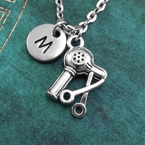 May include: Silver necklace featuring a hair dryer charm and a round charm with the letter M.