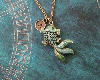 May include: A gold chain necklace with a green and gold fish charm and a small gold charm with the letter 'A' on it.