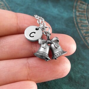 May include: Silver necklace with a charm of two wedding bells and a round disc with the letter C.