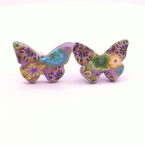 Peut inclure: Une paire de boucles d'oreilles en forme de papillon avec un motif floral dans des tons de violet, rose, jaune, bleu et vert.