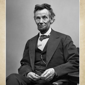 Puede incluir: Fotograf&iacute;a en blanco y negro de Abraham Lincoln, el 16&ordm; presidente de los Estados Unidos. Lleva un traje oscuro, una camisa blanca y una corbata de lazo oscura. Est&aacute; sentado y mirando directamente a la c&aacute;mara.