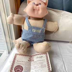 Peut inclure: Une poupée Koosas Cabbage Patch Kids vintage, avec un visage de chat aux yeux bleus et des cheveux blancs. La poupée porte une salopette en jean et un collier marron. Un certificat d'enregistrement Koosas est inclus.