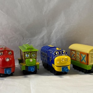 Puede incluir: Cuatro vagones de tren de juguete coloridos. El primero es rojo, el segundo es verde y marrón, el tercero es azul y amarillo, y el cuarto es amarillo y naranja. Cada vagón tiene un diseño y una cara únicos.