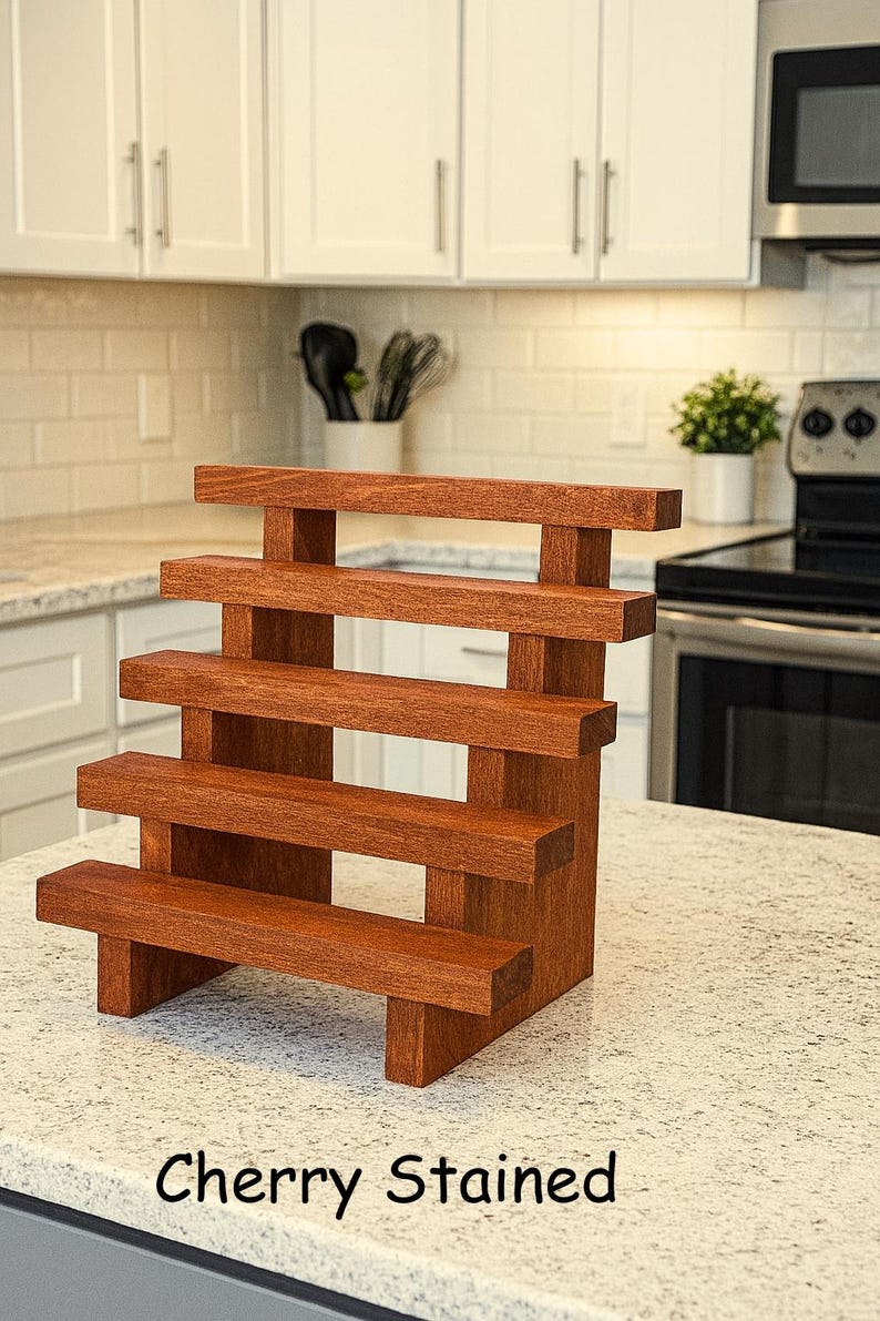 May include: A cherry-stained, wooden tiered display stand with four shelves. The stand is rectangular with a step design, ideal for showcasing items. The text "Cherry Stained" is visible at the bottom of the image.