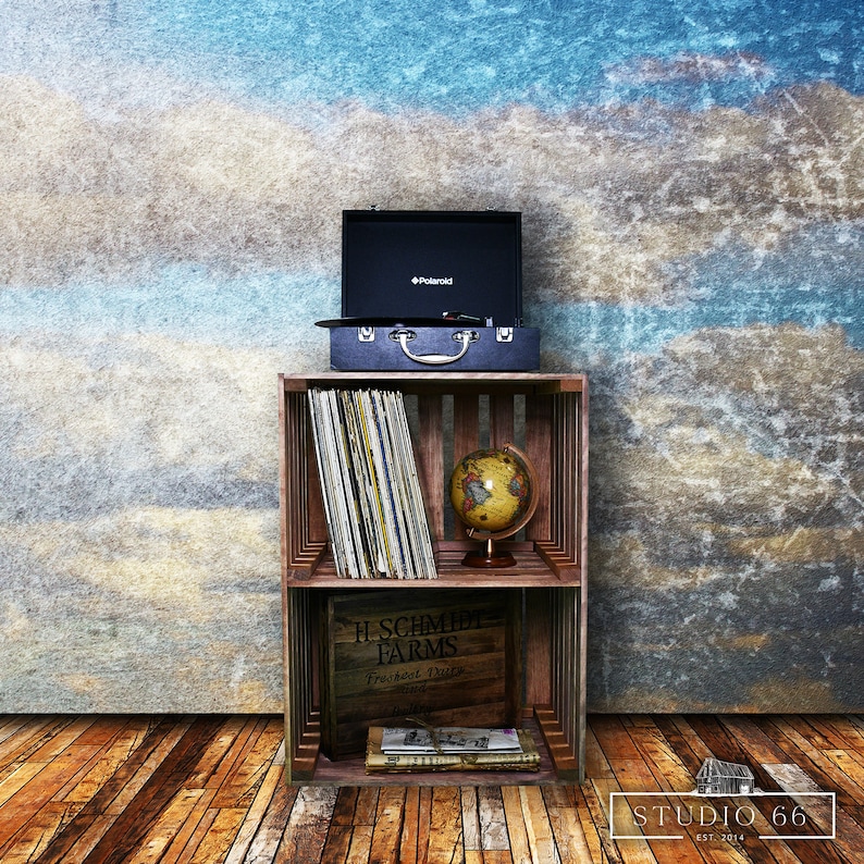 May include: A wooden crate shelf with two shelves, a vintage record player, a globe, and a box of records. The shelf is against a blue and brown textured wall. The text on the box reads "H. Schmidt Farms, Fresh Milk Dairy, Since 1912".