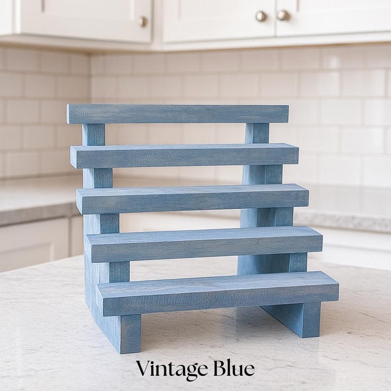 May include: A blue wooden display stand with five stepped levels. The stand is painted in a vintage blue color and has the words "Vintage Blue" printed at the bottom. The stand is designed to showcase items.