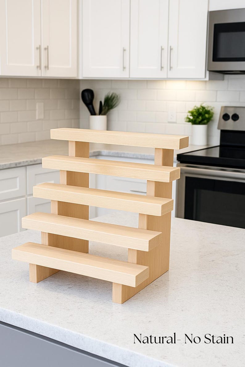 May include: A natural wood, multi-tiered display stand with five shelves. The stand is constructed from light-colored wood and features a simple, modern design. The text "Natural - No Stain" is visible at the bottom.