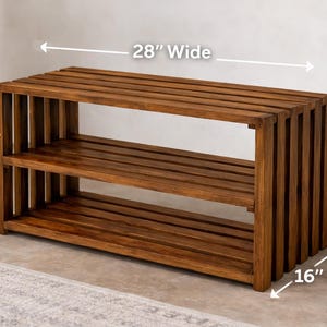 Może przedstawiać: Drewniany stojak na buty z dwiema p&oacute;łkami. Stojak ma 71 cm szerokości, 51 cm wysokości i 41 cm głębokości. Drewno ma ciepły, brązowy odcień. Konstrukcja posiada pionowe listwy po bokach i poziome listwy na p&oacute;łkach.