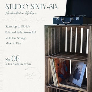 May include: A three-tier wooden record stand with a dark brown finish. The stand is made of reclaimed wood and has a rustic look. It is designed to hold up to 180 vinyl records. The stand is shown with a record player on top and records and a picture frame on the shelves. The text "Studio Sixty-Six" is visible on the stand.
